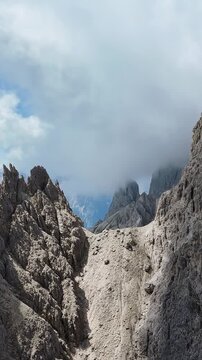 Cinematic aerial view flying through jagged rocky mountain peaks and misty clouds in dolomites alpine landscape.