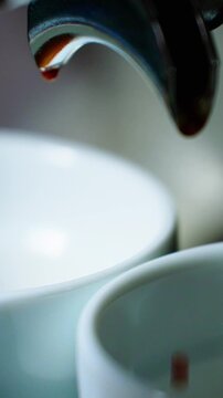 An espresso machine releases rich dark coffee that drips slowly into two waiting white cups. The setting is warm and inviting, perfect for a morning pick-me-up.