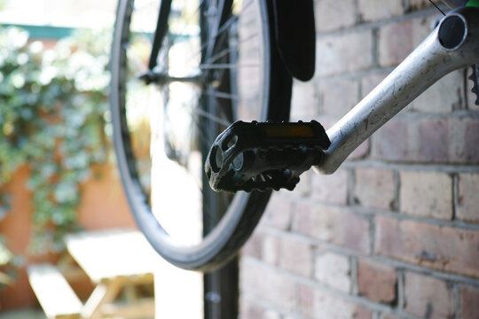 Black bicycle pedal attached to silver crank arm near brick wall