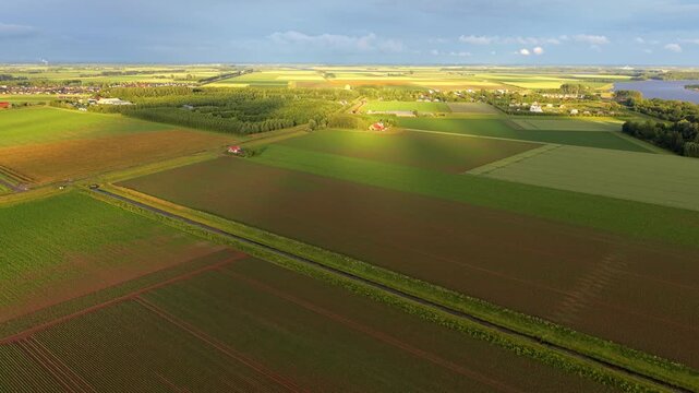 High angle horizontal aerial drone video clip of agricultural fields, farmhouse, Veerse Meer, Ruiterplaat, polder landscape, and warm sunset light, Zeeland, Netherlands, West Europe