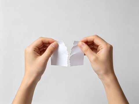 Hands tearing a piece of white paper in half