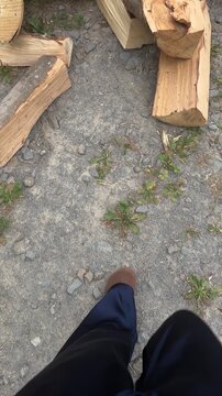 Person in brown shoes walking on gravel ground towards pile of chopped firewood logs for countryside lifestyle and winter heating concept
