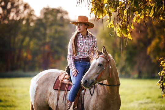 Woman rider resting on horse at autumn rural scenery. Cowgirl horseback riding in western style