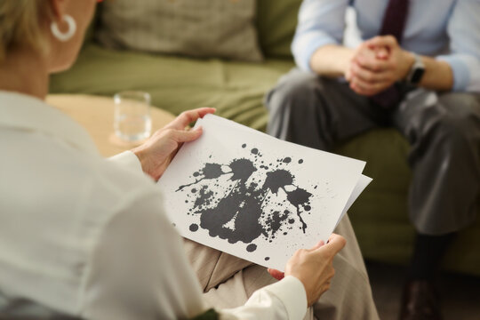 Middle aged Caucasian female psychologist holding Rorschach inkblot test card during therapy session with male patient. Image suitable for mental health and psychotherapy services