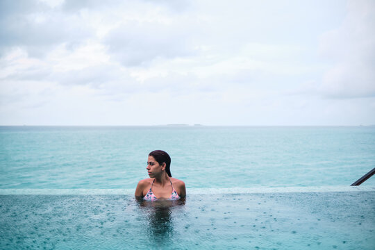 A white woman relaxing in an infinity pool overlooking the ocean