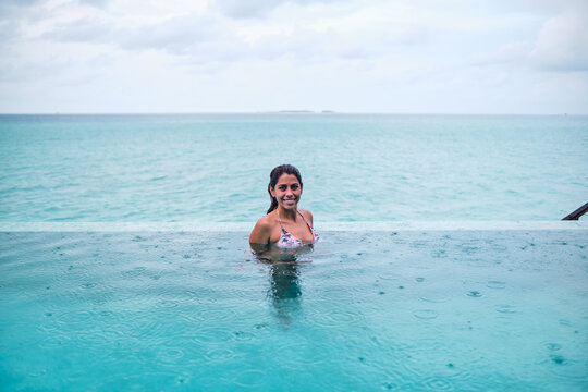 A white woman swimming in an infinity pool overlooking the ocean