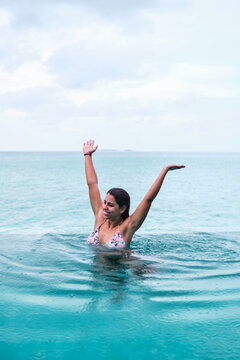 A white woman raises her arms swimming in an infinity pool