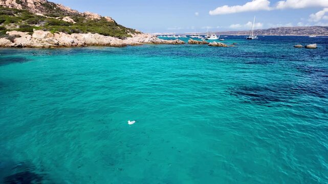 Panoramic view of the turquoise bay with a rocky coastline with yachts and boats off the coast of Spargi Island in the La Maddalena archipelago, Sardinia, Italy