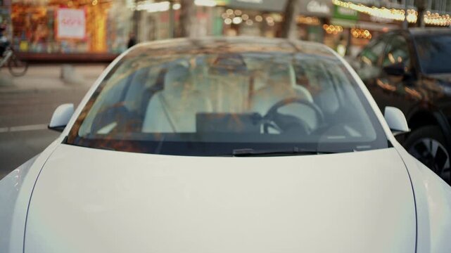 White electric vehicle parked on city street at evening.