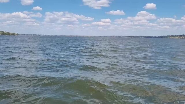 The camera shows a wide view of the river with gentle waves and clouds above. The scene captures the sunlight reflecting on the water.