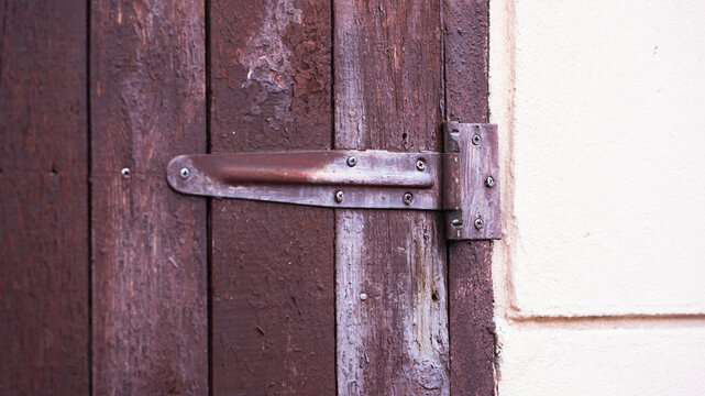 Close-up of a rusty metal strap hinge mounted on an old brown wooden door with peeling paint. Rustic architectural detail, vintage textures, background.