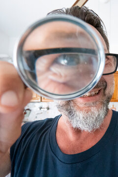 Man smiling and looking through a magnifying glass that enlarges his eye and glasses.