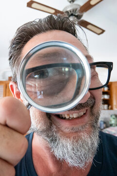 Man smiling and holding a magnifying glass to his eye in a playful close-up portrait.