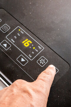 Hand pressing a digital appliance control panel showing temperature and fan settings on a black surface