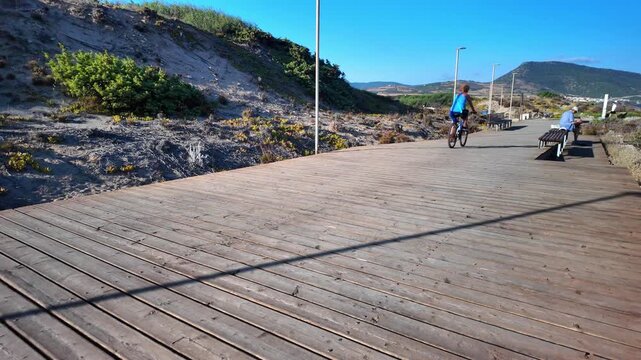 Woman in a blue blouse riding a bicycle along a wooden seaside promenade on a sunny day