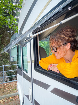 Woman leaning from an RV window smiling during a relaxed summer camper road trip by trees