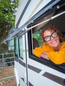 Woman smiling from a camper window wearing a yellow sweater during a relaxed outdoor road trip