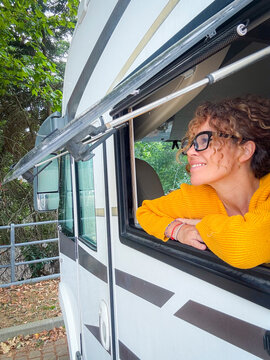 Woman smiling and leaning out of a camper van window wearing a yellow sweater, enjoying outdoors.