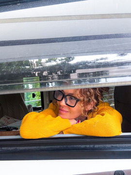 Woman in yellow sweater leaning on camper window, smiling and looking outside