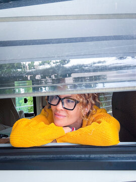 Woman in yellow sweater leaning on camper window smiling thoughtfully outdoors