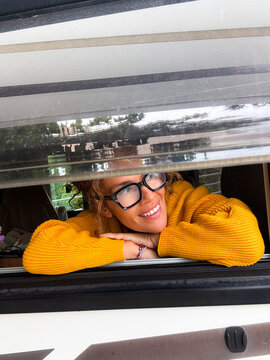 Woman in yellow sweater smiling and leaning out of a camper van window during road trip
