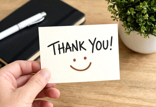 Hand holding a thank you card with smiley face on wooden desk workspace setting