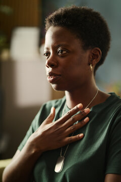 Young African American woman veteran holding hand over heart during therapy session, expressing vulnerability. Image suitable for mental health advocacy campaigns, vertical