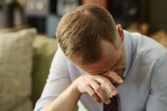 Middle aged Caucasian man crying and wiping tears with tissue, experiencing emotional breakdown. Image represents mental health struggles, suitable for therapy and counseling services