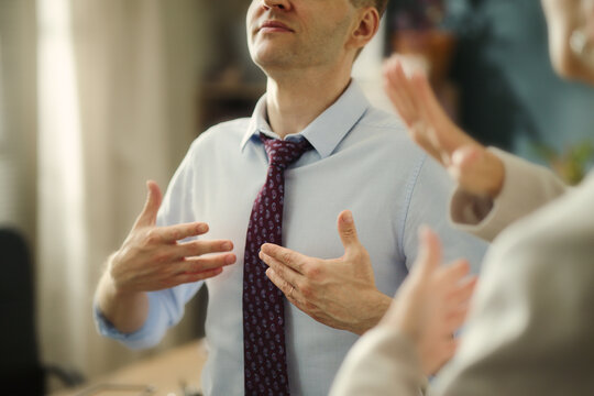 Middle aged Caucasian businessman using sign language to communicate with colleague in office. Image represents diversity and inclusion in corporate communication, close up