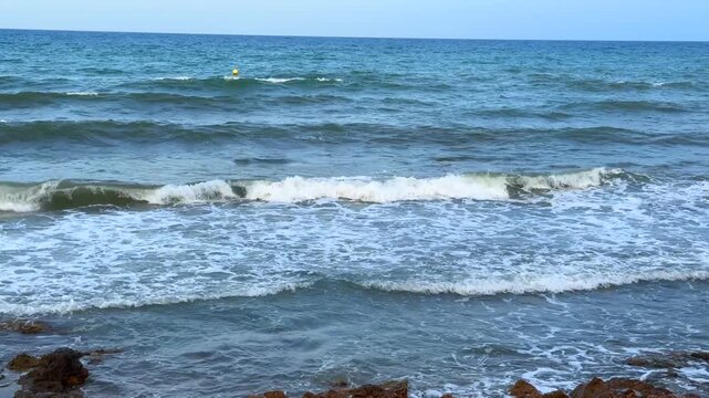 Sea waves rolling and breaking near shoreline with white foam on a sunny day in Orihuela Spain