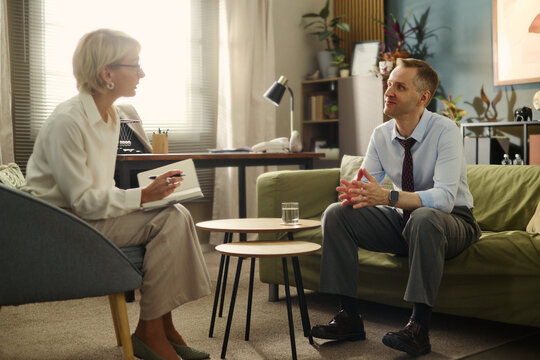Middle aged Caucasian man talking to female therapist during psychotherapy session. Image represents mental health support and is suitable for counseling services marketing