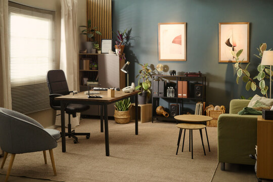 Empty modern home office interior showing desk with chair, shelving unit, and green sofa. Image suitable for remote work, hybrid workplace, and interior design marketing, wide shot