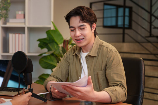 Asian man holding script while recording podcast in home studio