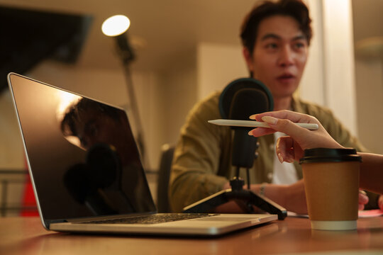 Laptop on table with podcaster speaking into microphone in studio