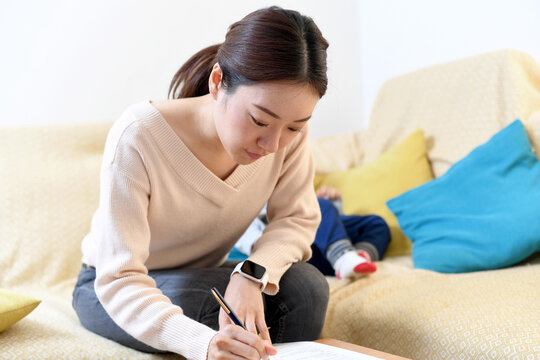 自宅のリビングで書類を書くアジア人の女性
