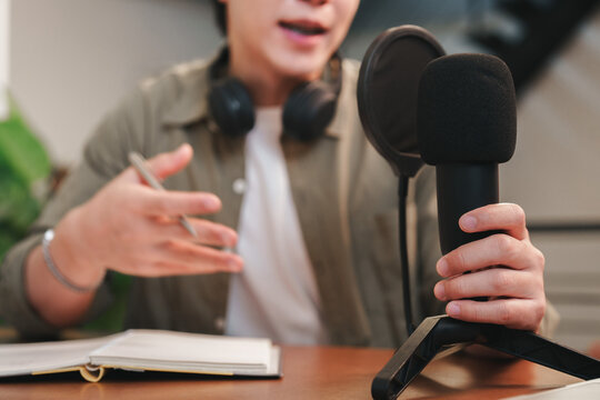 Asian man recording audio podcast with microphone at studio desk