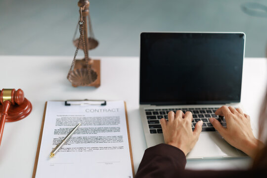 Legal professional hands typing on laptop, preparing contract paperwork, working in law office with justice scales and gavel on desk