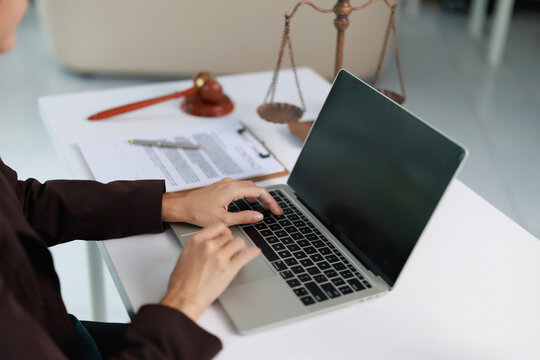 Legal professional using laptop for online research and drafting legal documents in an office setting, with scales of justice and gavel symbolizing law and order