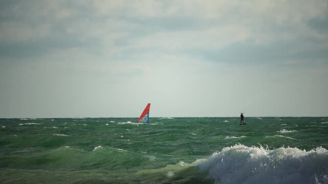 Windsurfing, Ocean, Water Sports: A lone windsurfer sails on the ocean under a cloudy sky.
