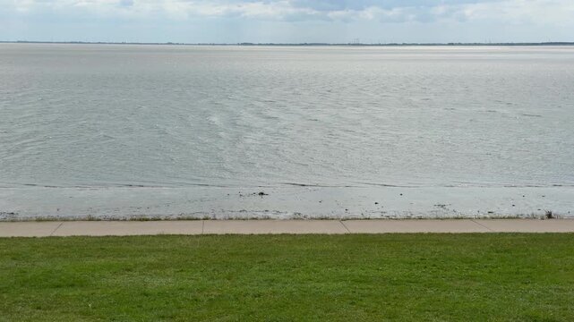 Calm water surface of the wadden sea with a green grass dike on a cloudy day in germany