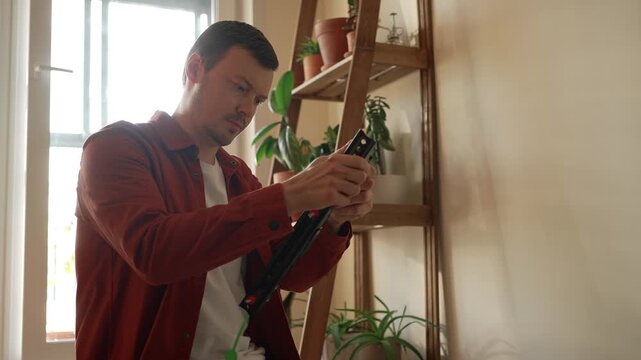 Concentrated man assembling a new television wall mount in his apartment, carefully reading the instruction manual and using a spirit level for a precise do it yourself setup