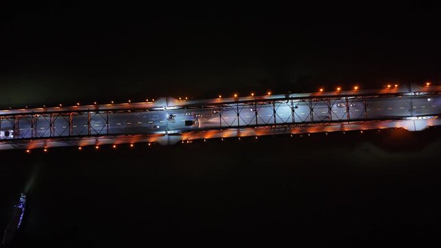 Aerial perspective of a brightly lit bridge at night, featuring moving vehicles and reflections on the water, highlighting urban development in Vietnam