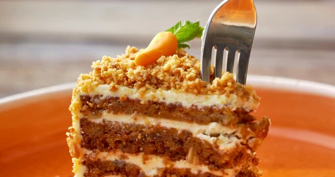 Macro detail view shows a fork slicing through moist carrot cake and thick cream layers beneath crunchy nut crumbs while a miniature carrot and fresh mint garnish the bright handcrafted dessert