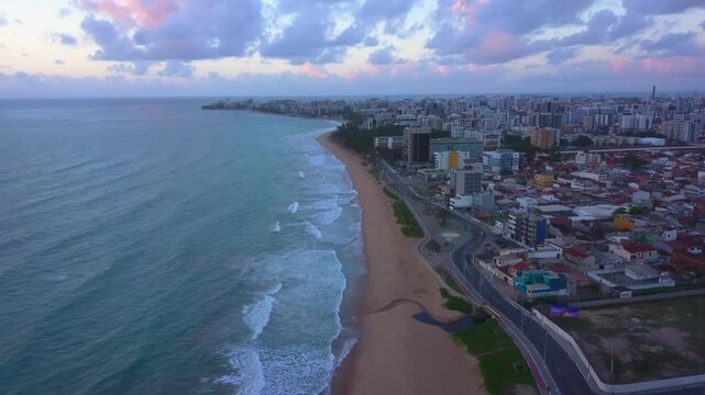 Aerial glide panning laterally along the coast of Macei&oacute; as pinkish sunset lights up the beach skyline. Shot in 4K at 25 fps.