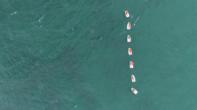 Overhead drone aerial row of small sailing dingles with orange sails flapping