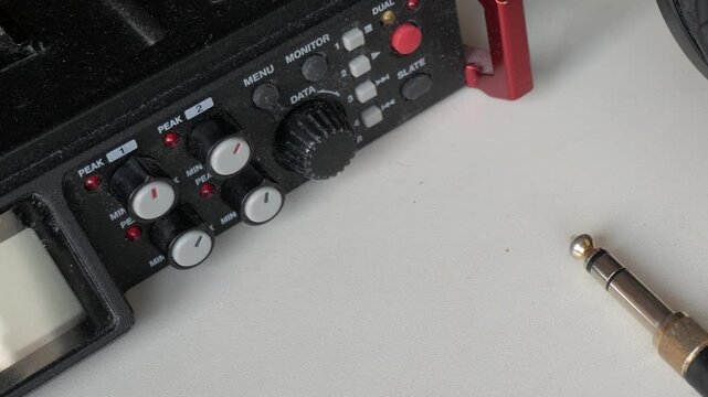 Audio recording gear on white table. Headphones and jack plug next to a portable recorder.