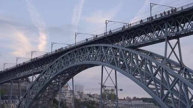 Static view looking up at the iron structure of the Dom Lu&iacute;s I bridge in Porto as pedestrians cross the upper deck during a clear morning. Shot in 4K at 25 fps.