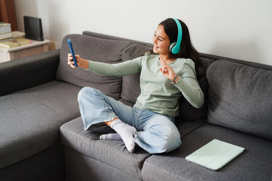 Female teen doing reel video for social media with smartphone while listening music with headphones - Technology and teenager lifestyle concept - Main focus on face