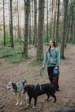 Woman standing with two dogs on leashes during an outdoor walk on a forest trail.
