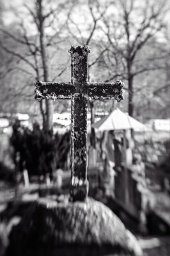 Old iron cross in cemetery. Black and white image. Selective focus, tilt shift, partly blurred. Ancient tombstone detail.